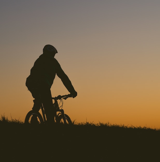 Schattenbild einer Person, die ein Fahrrad auf einem Feld während eines Sonnenuntergangs reitet