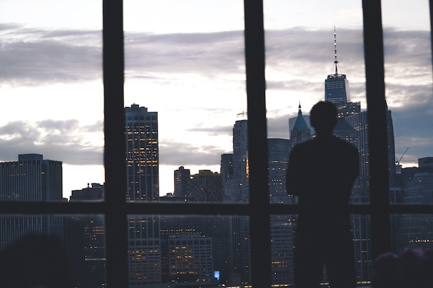 Schattenbild eines erfolgreichen männlichen Stehens eines Fensters mit Blick auf die Insel Manhattan