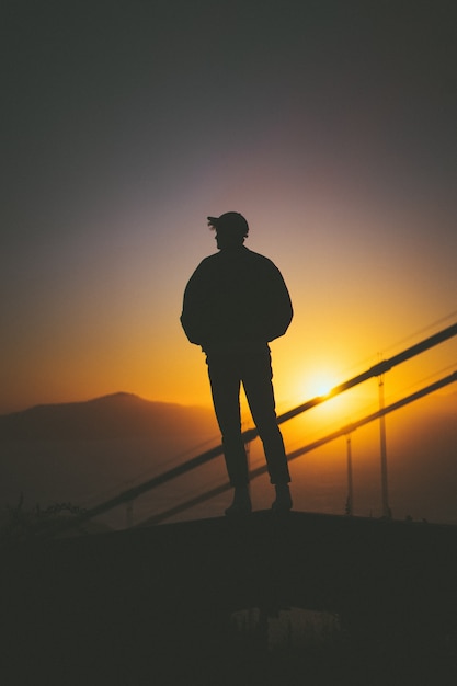 Schattenbild eines jungen Mannes, der auf der Treppe hinter Treppengeländern mit schönem Sonnenuntergangblick steht