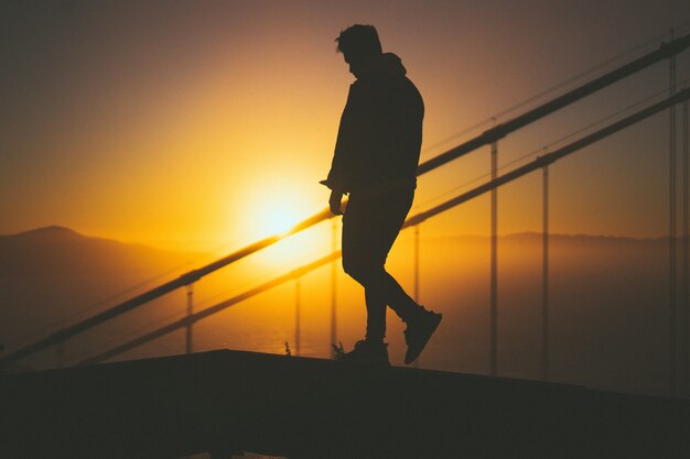 Schattenbild eines jungen Mannes, der auf der Treppe hinter Treppengeländern mit schönem Sonnenuntergangsblick geht