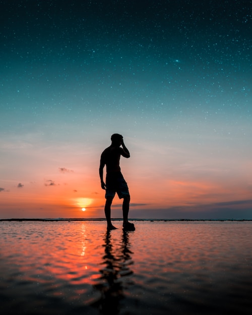 Schattenbild eines Mannes, der auf dem Wasser am Strand mit einem erstaunlichen Sonnenuntergang steht