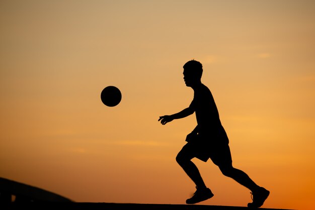 Schattenbild eines Mannes, der Fußball in der goldenen Stunde, Sonnenuntergang spielt.