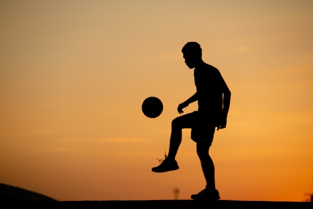 Schattenbild eines Mannes, der Fußball in der goldenen Stunde, Sonnenuntergang spielt.