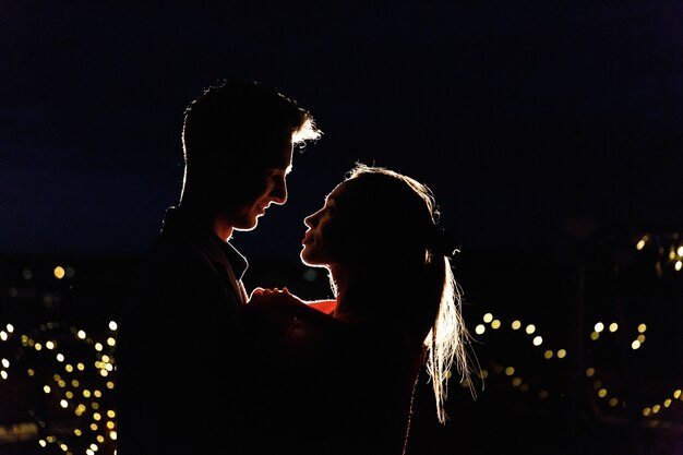 Schattenbilder eines reizenden jungen Paares, das auf der Dachspitze in der Nacht steht
