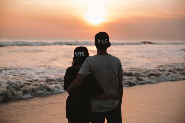Schattenbildporträt des jungen romantischen Paares, das auf dem Strand geht. Mädchen und ihr Freund posieren am goldenen bunten Sonnenuntergang. Sie umarmen sich und träumen