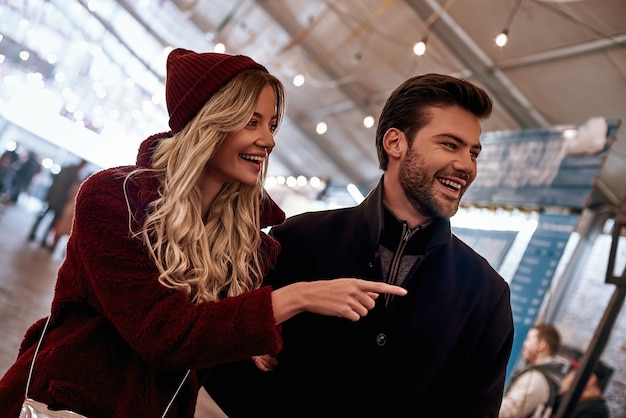 Schau dir dieses an. glückliches junges fröhliches paar, das auf dem straßenlebensmittelmarkt herumläuft. herbstsaison, blonde frau mit roter mütze, ihr freund lacht, sie sind auf dem straßenmarkt.