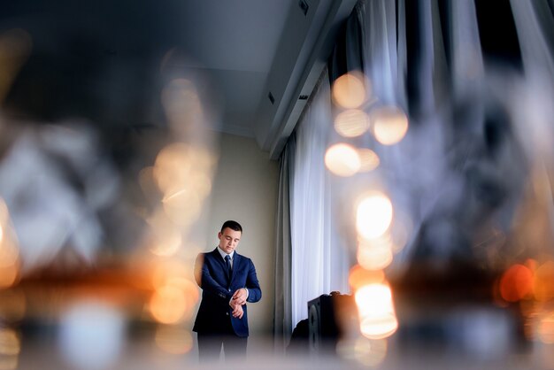 Schauen Sie hinter den Gläsern mit Whisky auf den hübschen Bräutigam, der vor einem Fenster steht