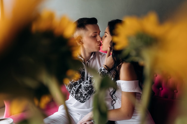 Schauen Sie hinter einem Blumenstrauß Sonnenblumen auf küssende Hochzeitspaare