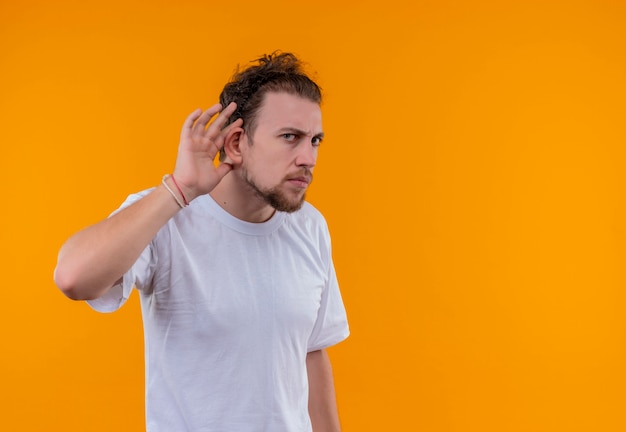 Schauender junger Mann, der weißes T-Shirt trägt, das hörgeste auf lokalem orange Hintergrund hört