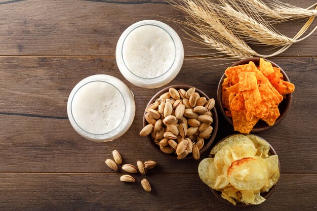 Schaumbier in Gläsern mit Pistazie, Weizenähren, Pommes-Draufsicht auf einem Holztisch