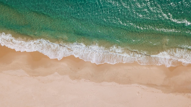 Schaumige Wellen und Sandstrand von oben