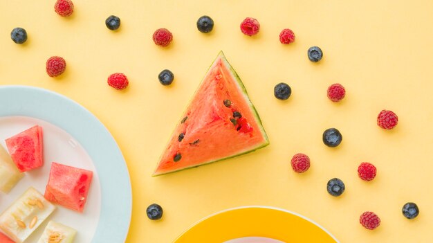 Scheibe der Wassermelone mit Blaubeeren und Himbeeren auf gelbem Hintergrund