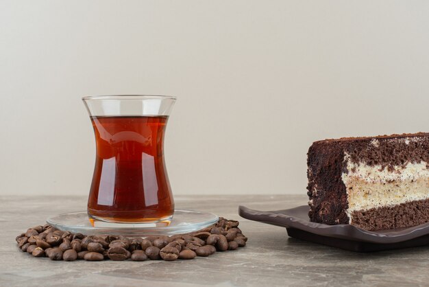 Scheibe Schokoladenkuchen, Kaffeebohnen und Glas Tee auf Marmortisch.