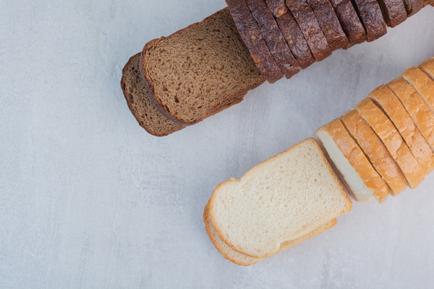 Scheiben frisches Weiß- und Schwarzbrot auf Marmorhintergrund.