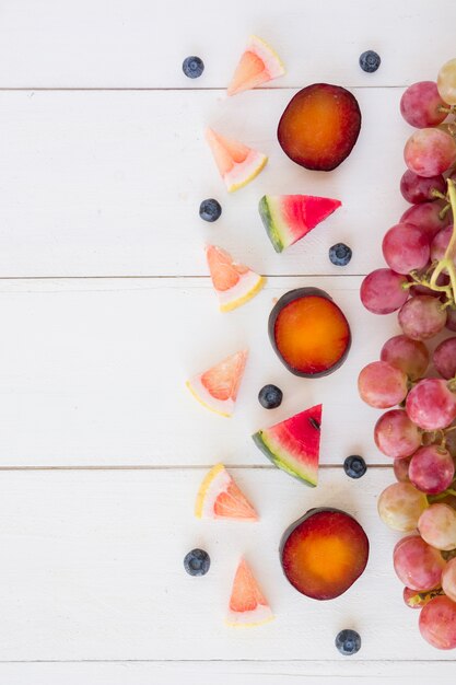 Scheiben Grapefruit Wassermelone; Blaubeeren; Pflaume und Trauben auf weißem Holzschreibtisch