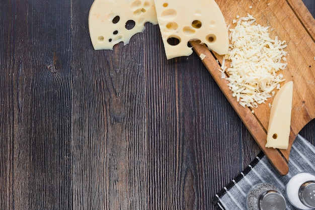 Scheiben und geriebener Maasdamkäse auf hölzernem Brett über dem schwarzen Schreibtisch