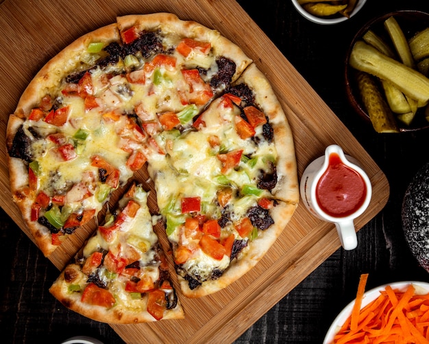Scheiben vegetarische Pizza mit Basilikum, Tomaten und Paprika auf einem Holztablett