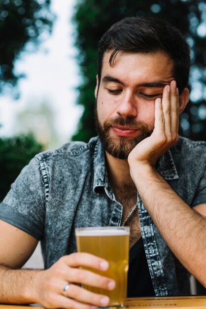 Schläfriger Mann, der Glas Bier hält