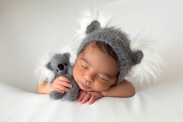 Schlafender Säugling, der friedlich kleines Neugeborenes mit niedlichem grauem Hut und Spielzeugbär legt