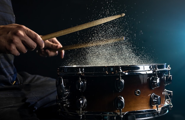 Schlagzeuger mit trommelstöcken, die snare-drum mit spritzwasser auf schwarzem hintergrund unter studiobeleuchtung schlagen.