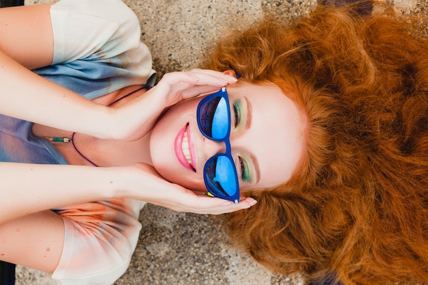 Schlanke Frau des jungen Hipster-Ingwers, die am Pool liegt, Blick von oben, bunte Haare bunt, blaue Sonnenbrille, Sportart, Sommersprossen, Muttermale, entspannt, glücklich, verspielt, cooles Outfit, lächelnd, sinnlich