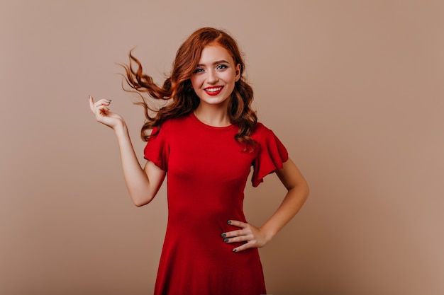 Schlanke kaukasische Frau im roten Kleid lachend. Wunderschönes Ingwermädchen, das mit ihren Haaren während des Fotoshootings spielt.
