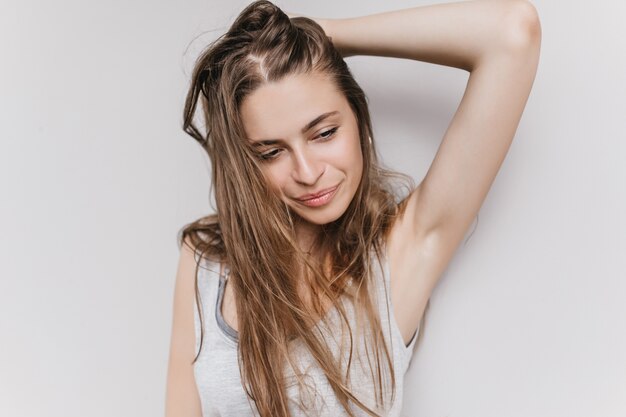 Schlanke wundervolle Dame, die mit ihren langen Haaren spielt und wegschaut. Innenfoto des ekstatischen kaukasischen Mädchens lokalisiert mit inspiriertem Gesichtsausdruck.