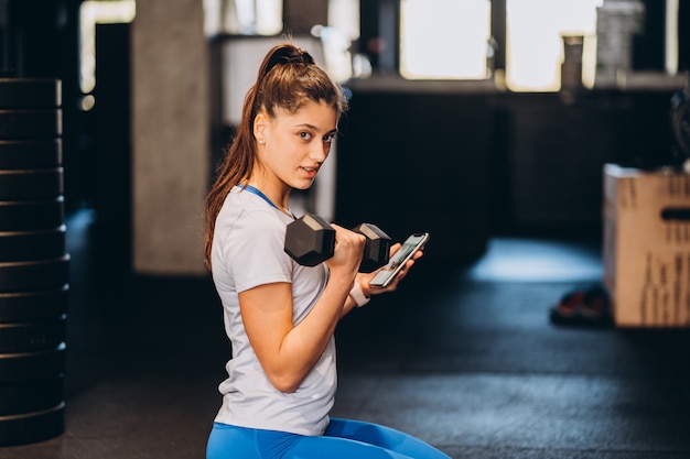 Schlankes sportliches Mädchen führt körperliche Übungen mit Hanteln im Fitnessstudio durch.