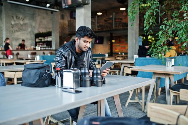 Schlauer junger asiatischer Mannfotograf, der mit Tablette beim Sitzen am Café arbeitet