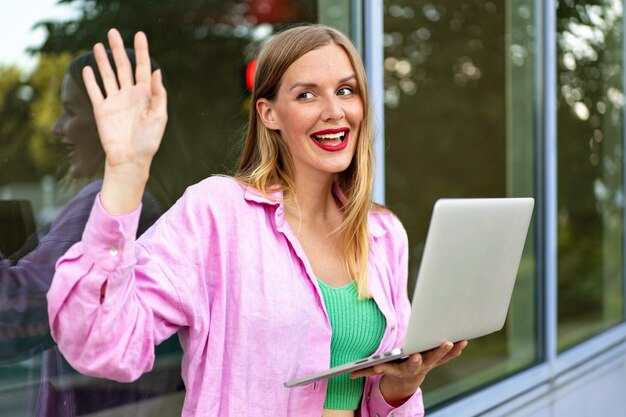 Schließen Sie das horizontale Bild einer blonden, stylischen Frau, die ihren Laptop benutzt, helles Make-up, positive Stimmung, Arbeit und Studium.