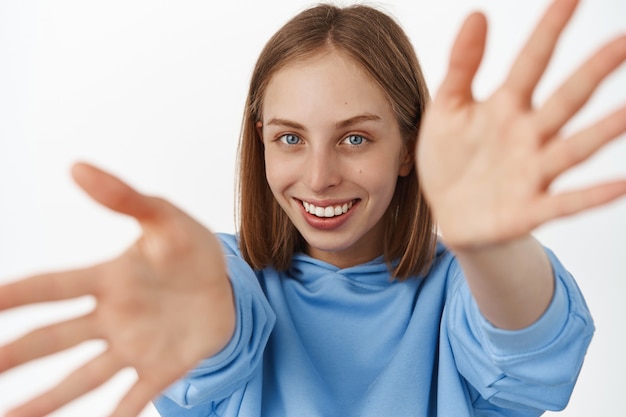 Kostenloses Foto schließen sie das porträt einer schönen blonden frau, die sich die hände ausstreckt, etwas hält oder berührt, sorglos lächelt, verträumt nach vorne blickt und in blauem hoodie steht. konzept der glücklichen menschen.