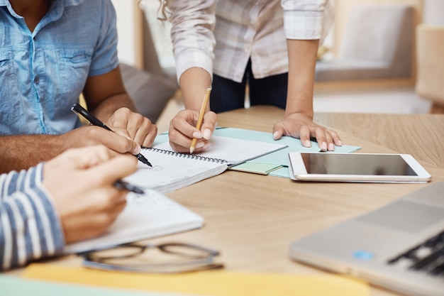 Schließen Sie Detail des Teams, das o neues Projekt im Coworking Space arbeitet, Ideen schreibt, Grafiken durch Tablet und Laptop durchschaut. Teamwork, Geschäftskonzept.