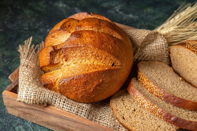 Schließen Sie die Ansicht des Ganzen und schneiden Sie frisches Schwarzbrot auf Handtuch in einer braunen Holzkiste auf dunkler Mischfarbenoberfläche