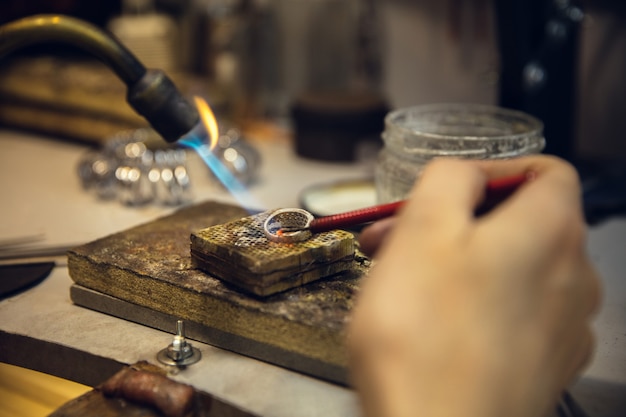 Schließen Sie die Hände des Juweliers, der Goldschmiede, die mit professionellen Werkzeugen aus goldenem Ring mit Edelstein machen