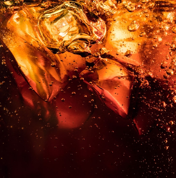 Schließen Sie herauf Ansicht der Eiswürfel im dunklen Cola-Hintergrund. Textur des kühlenden süßen Sommergetränks mit Schaum und Makroblasen an der Glaswand. Zischen oder Schweben bis zur Oberfläche.