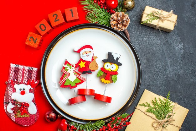 Schließen Sie herauf Ansicht des Essteller-Dekorationszubehörs Tannenzweige und nummeriert Weihnachtssocke auf einer roten Serviette neben Geschenk auf einem schwarzen Tisch