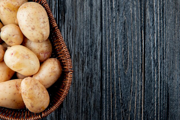 Schließen Sie herauf Ansicht des Korbs mit Kartoffeln auf der linken Seite und hölzernem Hintergrund mit Kopienraum