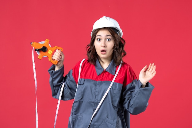 Kostenloses Foto schließen sie herauf ansicht des überraschten weiblichen architekten in der uniform, die schutzhelm mit maßband auf roter wand trägt