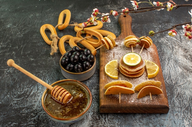 Schließen Sie herauf Ansicht von Fruchtpfannkuchenplätzchen nahe Honig in einer Schüssel und schwarzen Kirschen auf grauem Tisch