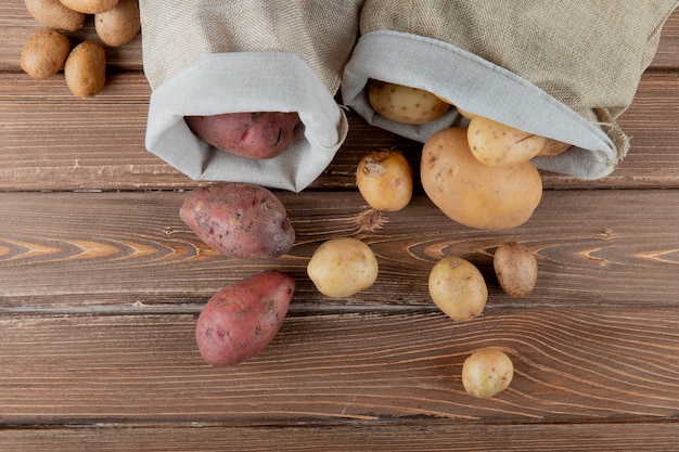 Schließen Sie herauf Ansicht von Kartoffeln, die aus Säcken auf hölzernem Hintergrund mit Kopienraum verschütten