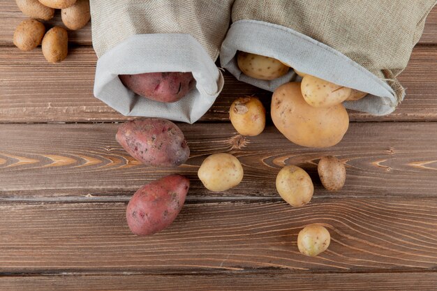 Schließen Sie herauf Ansicht von Kartoffeln, die aus Säcken auf hölzernem Hintergrund mit Kopienraum verschütten