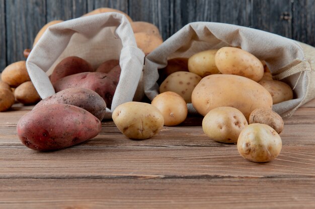 Schließen Sie herauf Ansicht von Kartoffeln, die aus Säcken auf Holzoberfläche und Hintergrund mit Kopienraum verschüttet werden