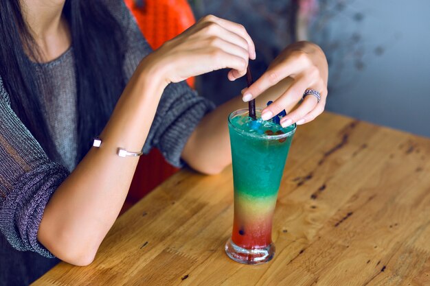 Schließen Sie herauf Bild der Frau, die leckeren bunten regenbogengeschmackvollen alkoholischen süßen Cocktail hält, Sommerfestzeit.