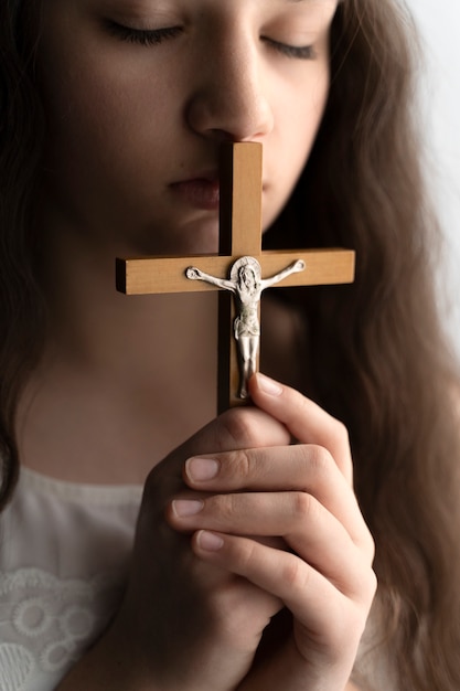 Schließen Sie herauf christliches Mädchen, das mit Kruzifix betet