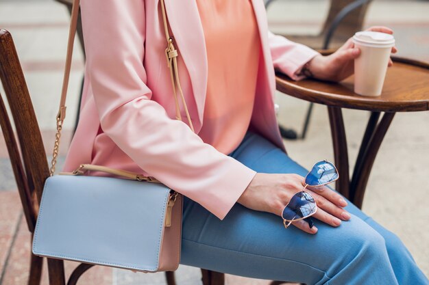 Schließen Sie herauf Details des Zubehörs der stilvollen Frau, die im Café sitzt, Sonnenbrille, Handtasche, rosa und blaue Farben, Frühlingssommer-Modetrend, eleganter Stil, Kaffee trinkend