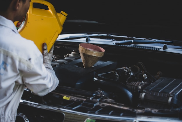 Schließen Sie herauf die Automechanikerhand, die frisches Öl in Automotor an der Autoreparaturgarage gießt und ersetzt. Automobilwartung und Industriekonzept