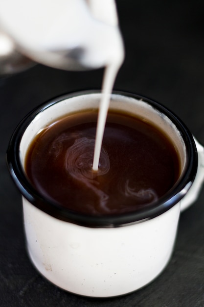 Schließen Sie herauf die Milch, die in schwarzen Kaffee gegossen wird