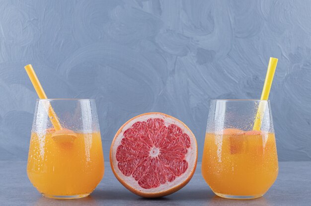 Schließen Sie herauf Foto von frisch gemachtem Orangensaft mit reifer Grapefruit auf grauem Hintergrund.