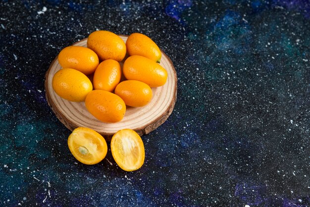 Schließen Sie herauf Foto von saftigen Kumquats auf Holzbrett über blauer Oberfläche