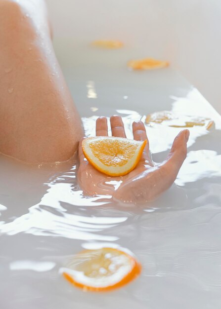 Schließen Sie herauf Frau, die mit Orangenscheiben im Wasser badet